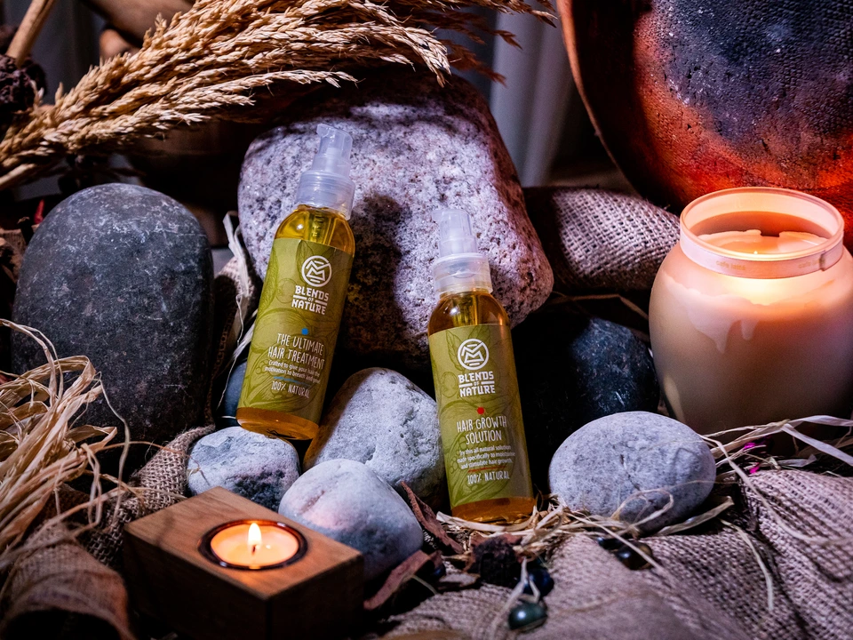 Hair-care products arranged among stones, plants, and a lit candle