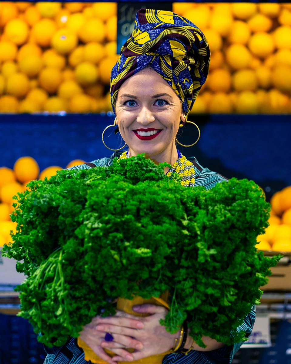 Woman holding a bunch of green vegetables at a produce display