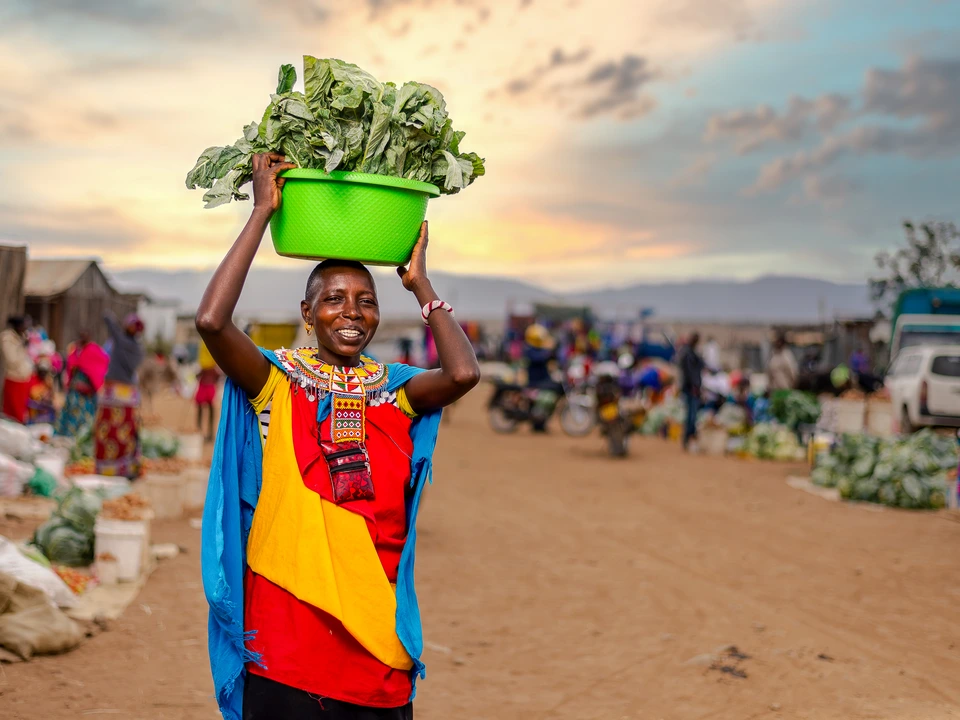 A person carrying a green basket through a bustling outdoor market