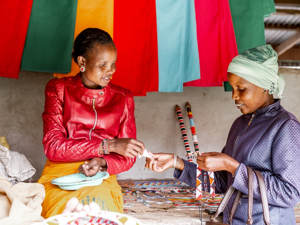 Two women working together at a sewing table with colourful fabric
