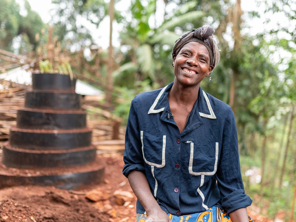 Woman standing beside stacked cooking pots in a green outdoor setting