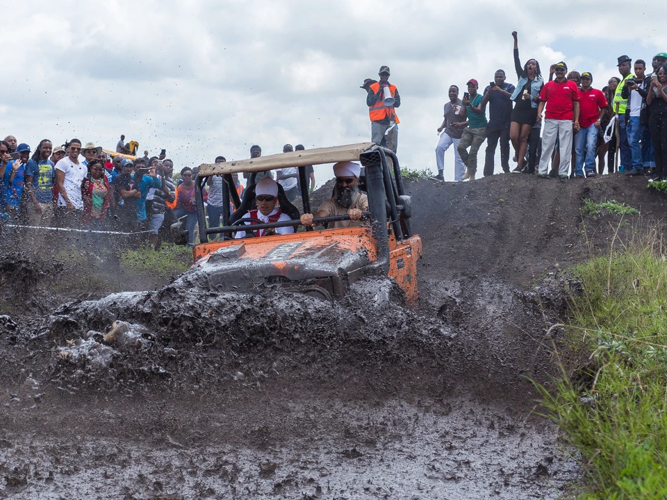 Off-road vehicle driving through a muddy track with spectators watching