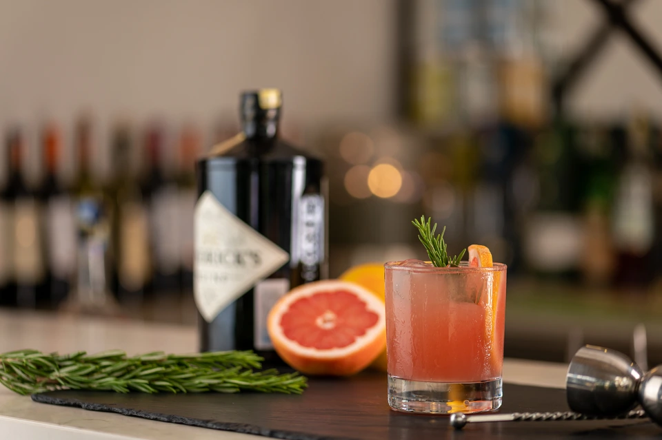 Cocktail beside a grapefruit and bottles on a bar