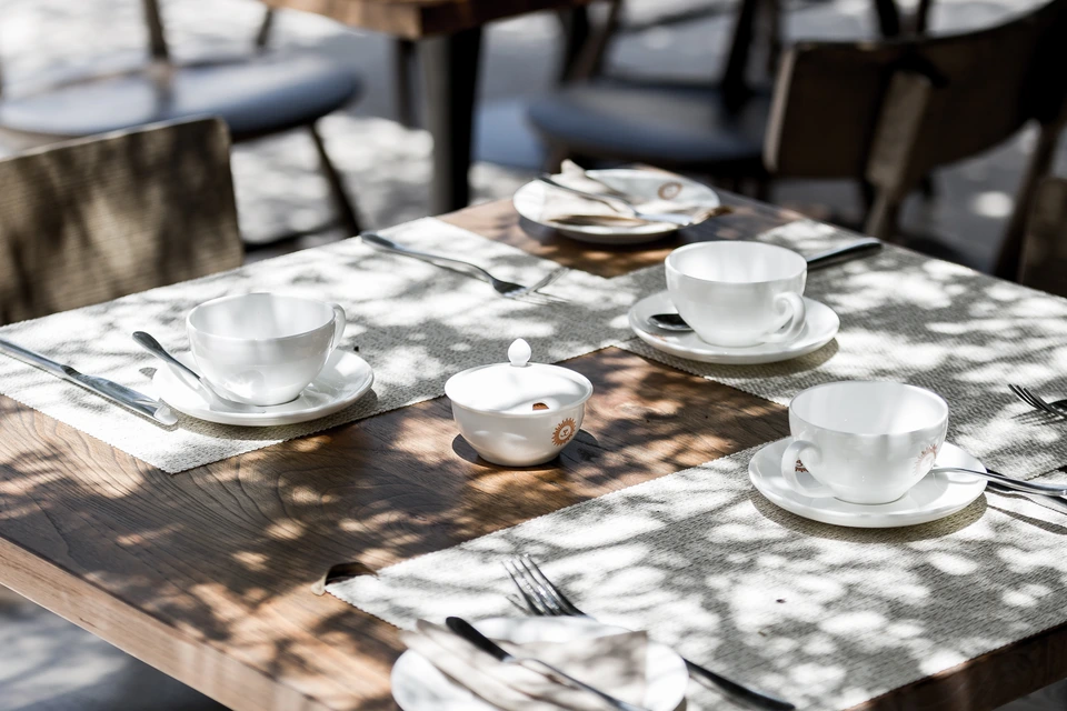 Restaurant table set beneath dappled light and leafy shadows