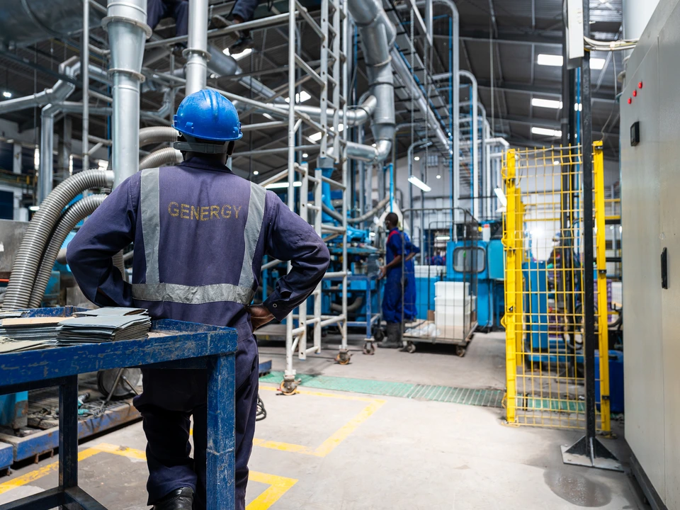 Worker in protective clothing standing beside factory pipework