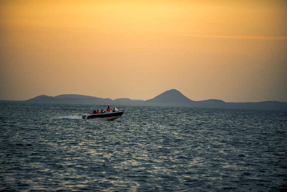 Small boat crossing the sea with distant islands beneath a warm sky