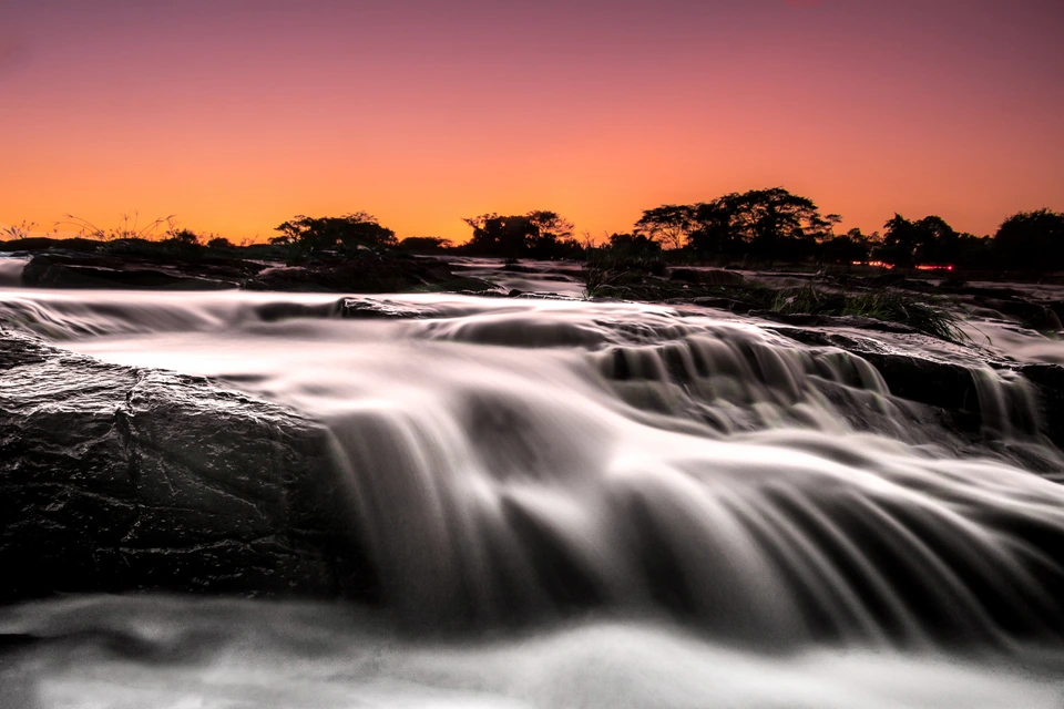 Flowing river cascading across rocks beneath a colourful evening sky