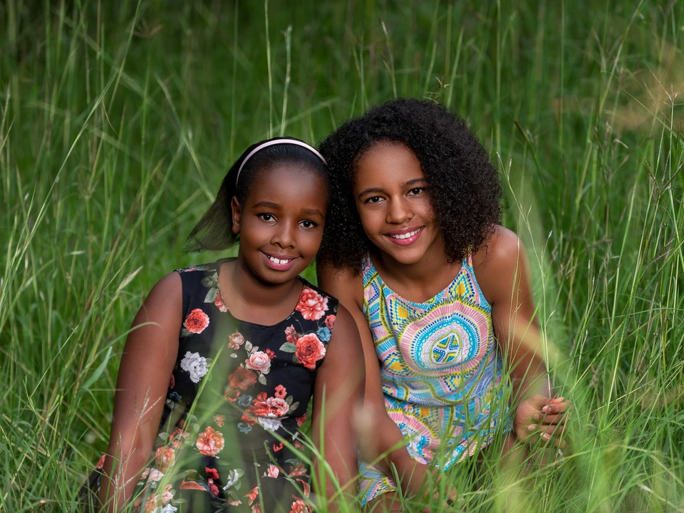 Two women sitting closely together in long green grass