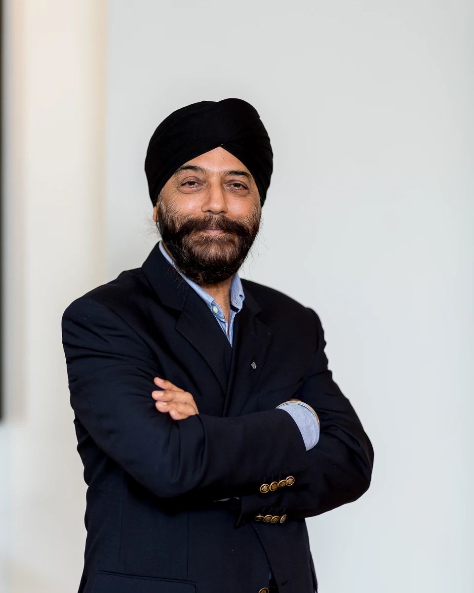 Man in a black suit and turban standing with folded arms