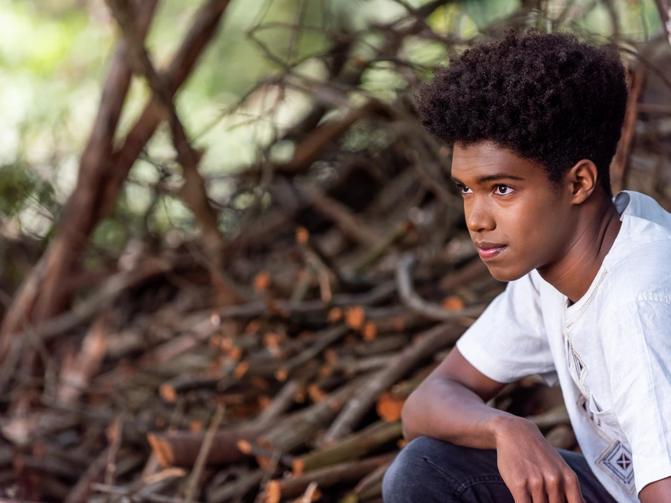 Young man seated outdoors beside textured tree roots